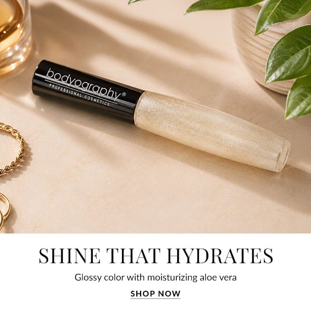 Advertising banner for a hydrating lip gloss; beige-glossy tube labeled Bodyography on a light beige surface with greenery in the corner.